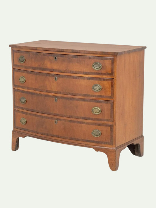 A curved-front wooden chest of drawers with five drawers, brass oval handles, and keyholes, shown on a light off-white background.