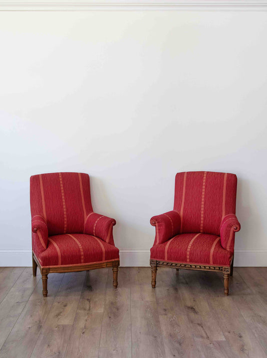 Two matching red striped armchairs with wooden frames, placed side by side on a light wood floor against a plain white wall.