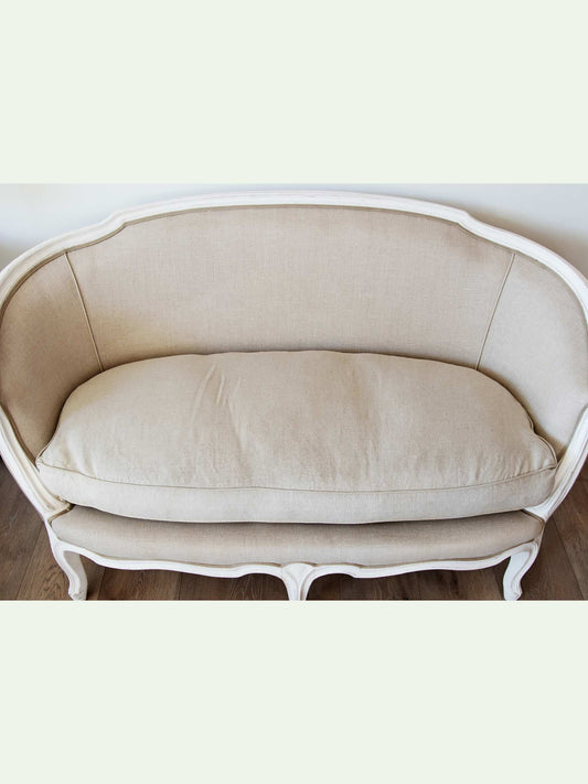 A vintage-style upholstered loveseat with a cream beige fabric cushion and a white carved wooden frame, shown against a light background.