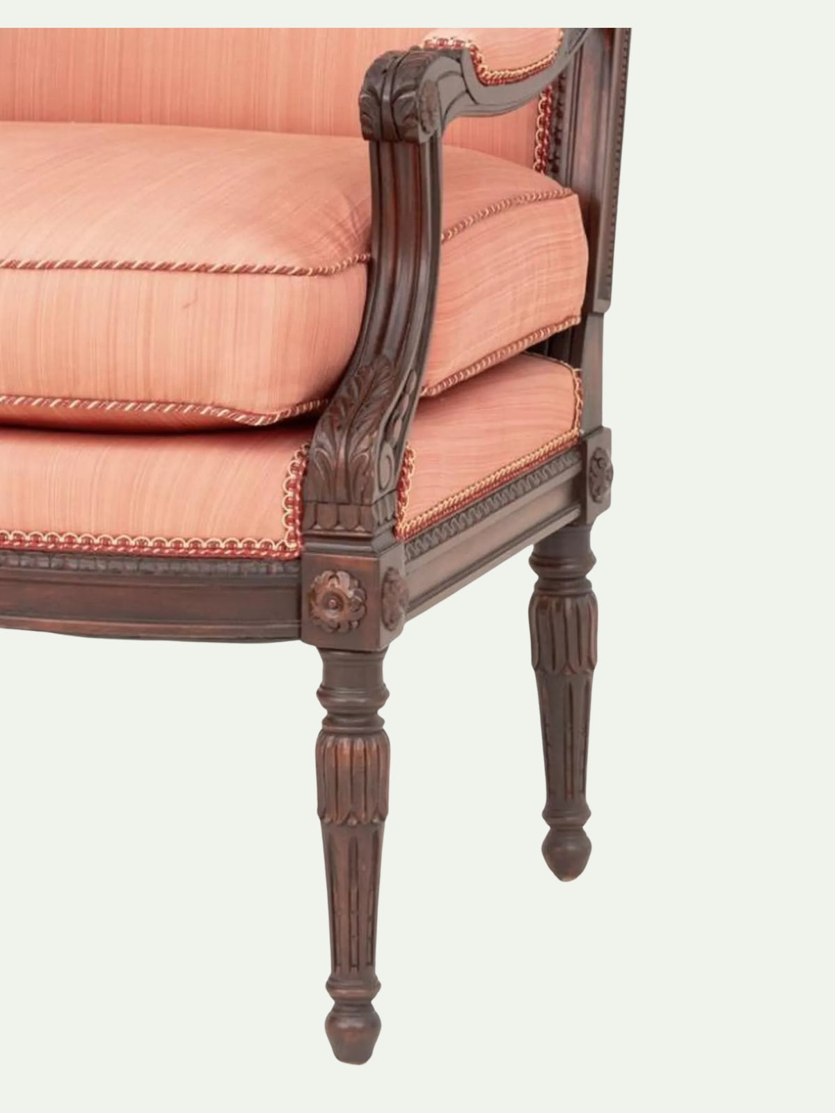 Close-up of an antique-style upholstered armchair with peach-pink striped fabric cushions and a carved dark brown wooden frame, shown against a light off-white background.