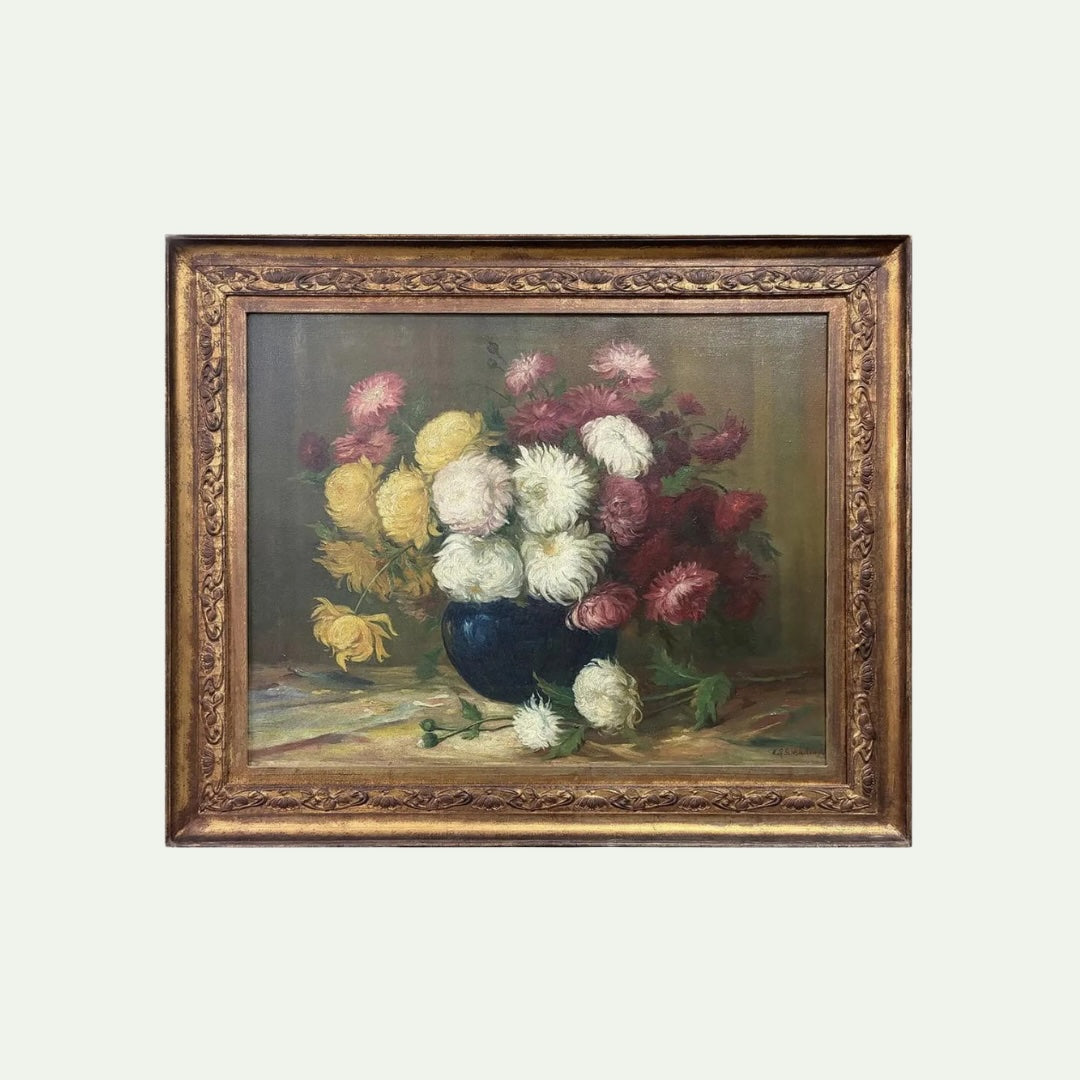 A framed still life oil painting depicting a bouquet of chrysanthemums in a dark blue vase, surrounded by a detailed antique-style gold frame, set against a solid off-white background.