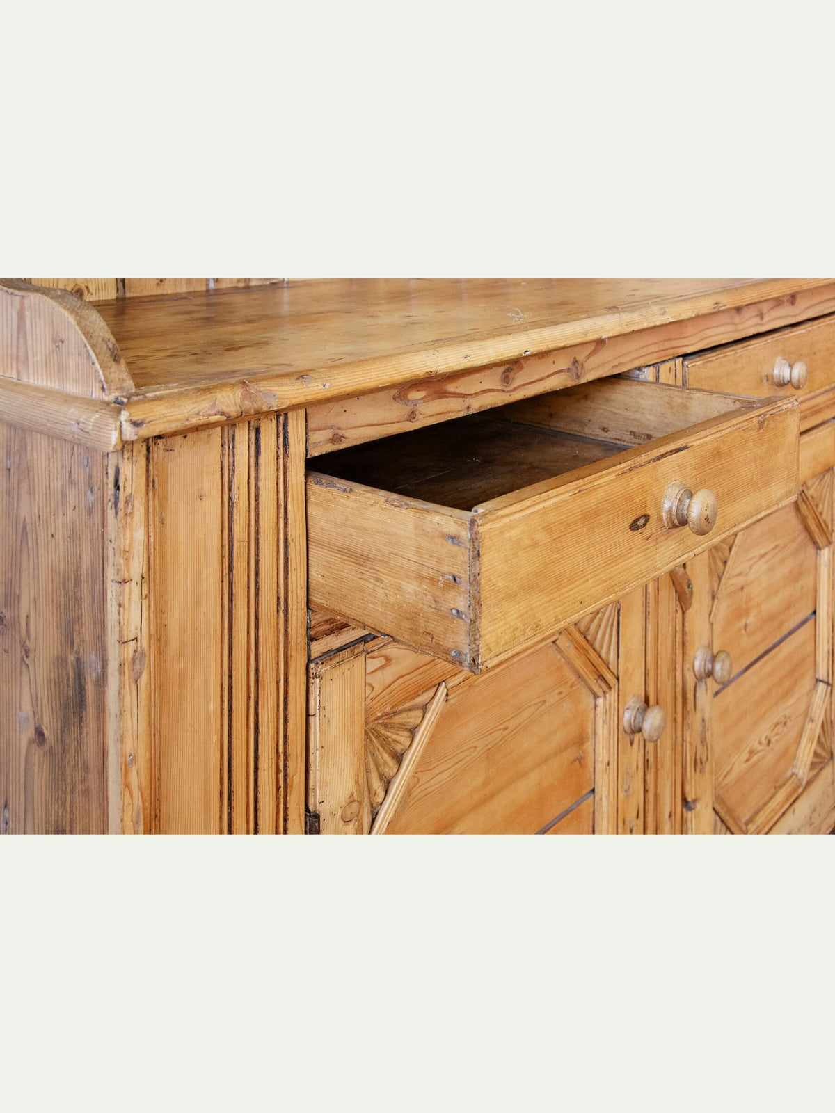 Close-up of a rustic light brown wooden cabinet with one drawer pulled open, showing natural wood grain and round metal knobs against a light gray background.
