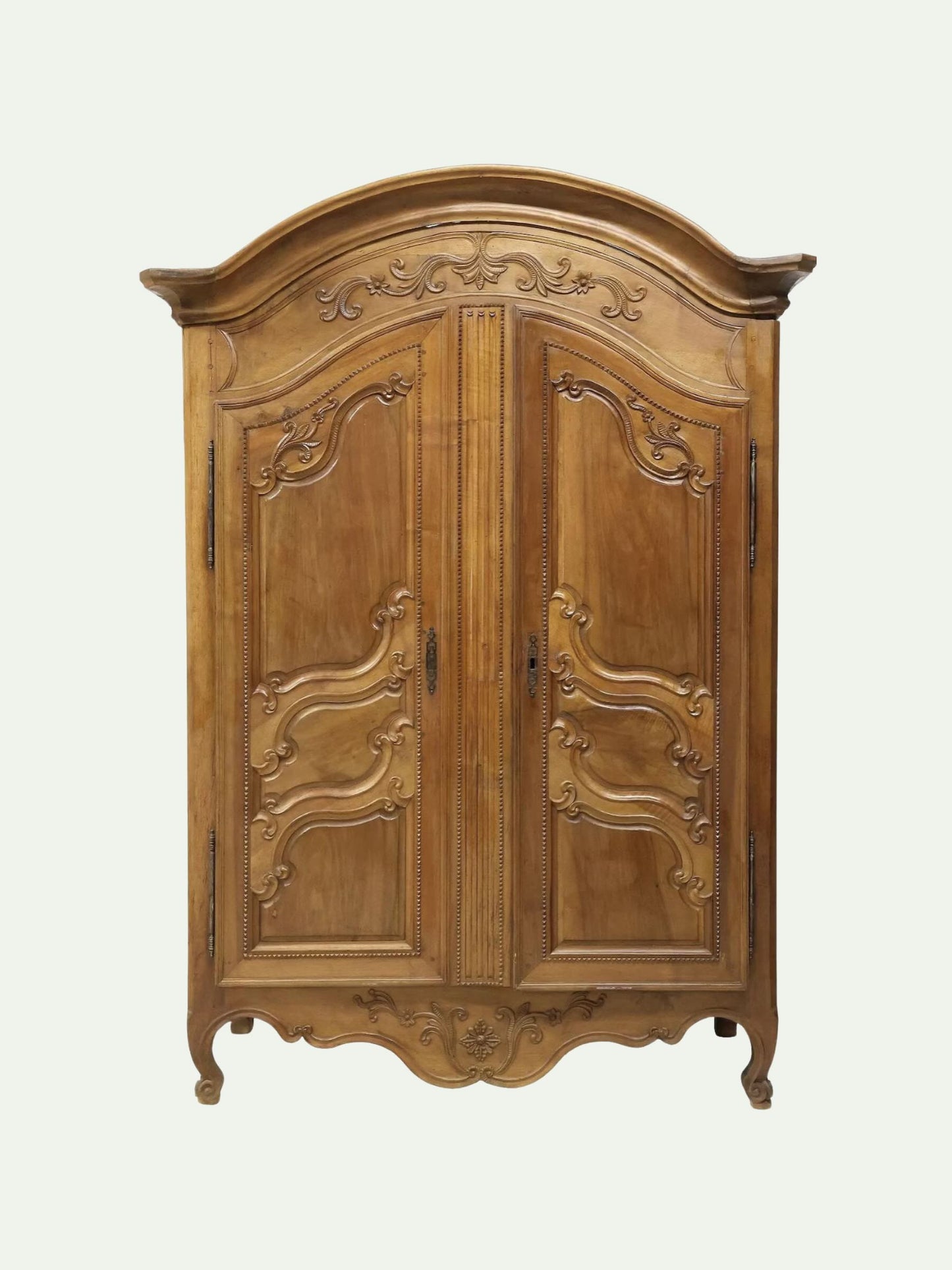 An antique-style wooden armoire cabinet with ornate carved details, featuring two doors, dark metal handles, and curved legs, shown against a plain off-white background.