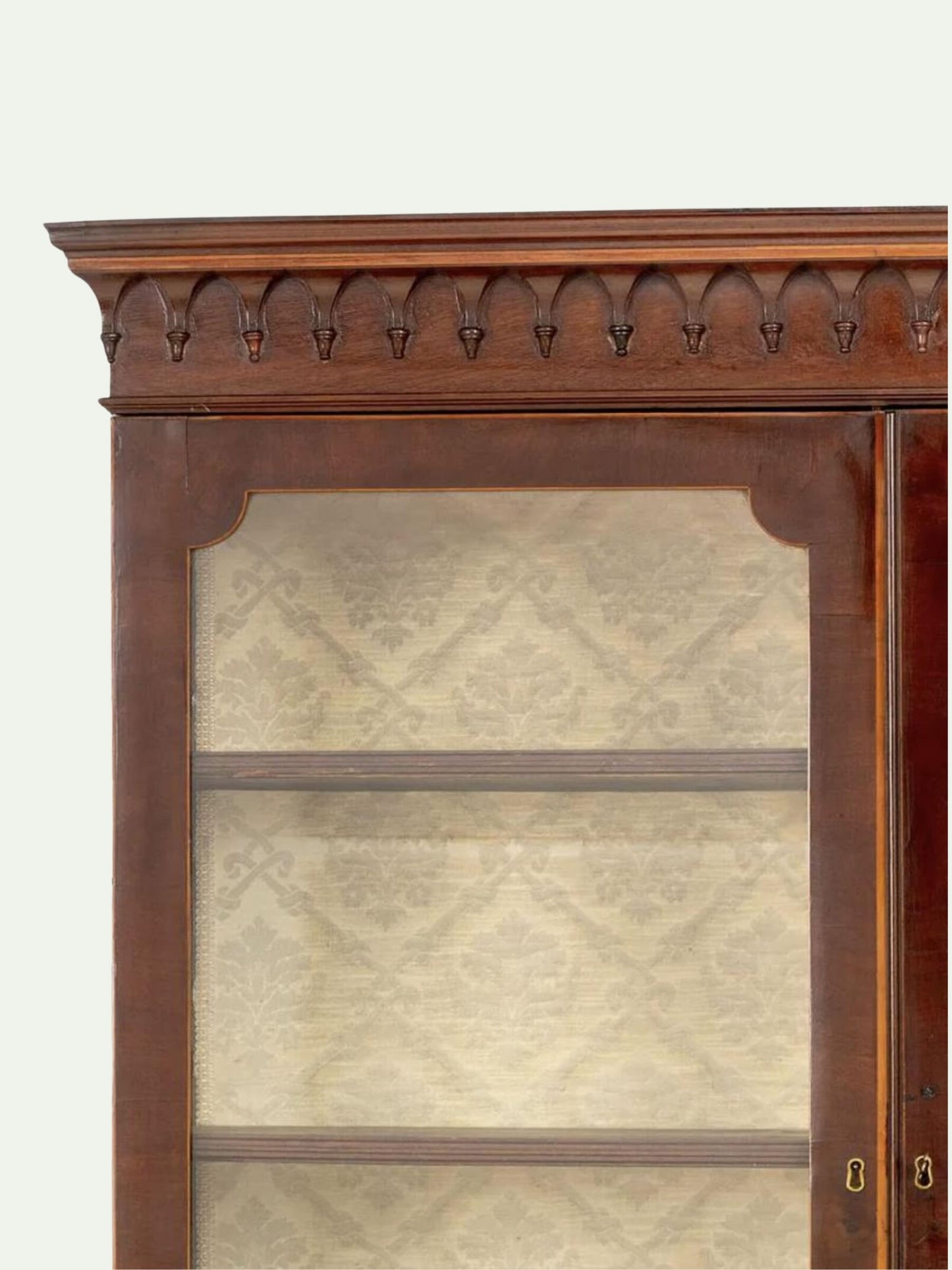 Close-up of a dark reddish-brown wooden display cabinet with a decorative carved top frame and glass doors showing patterned beige lining.