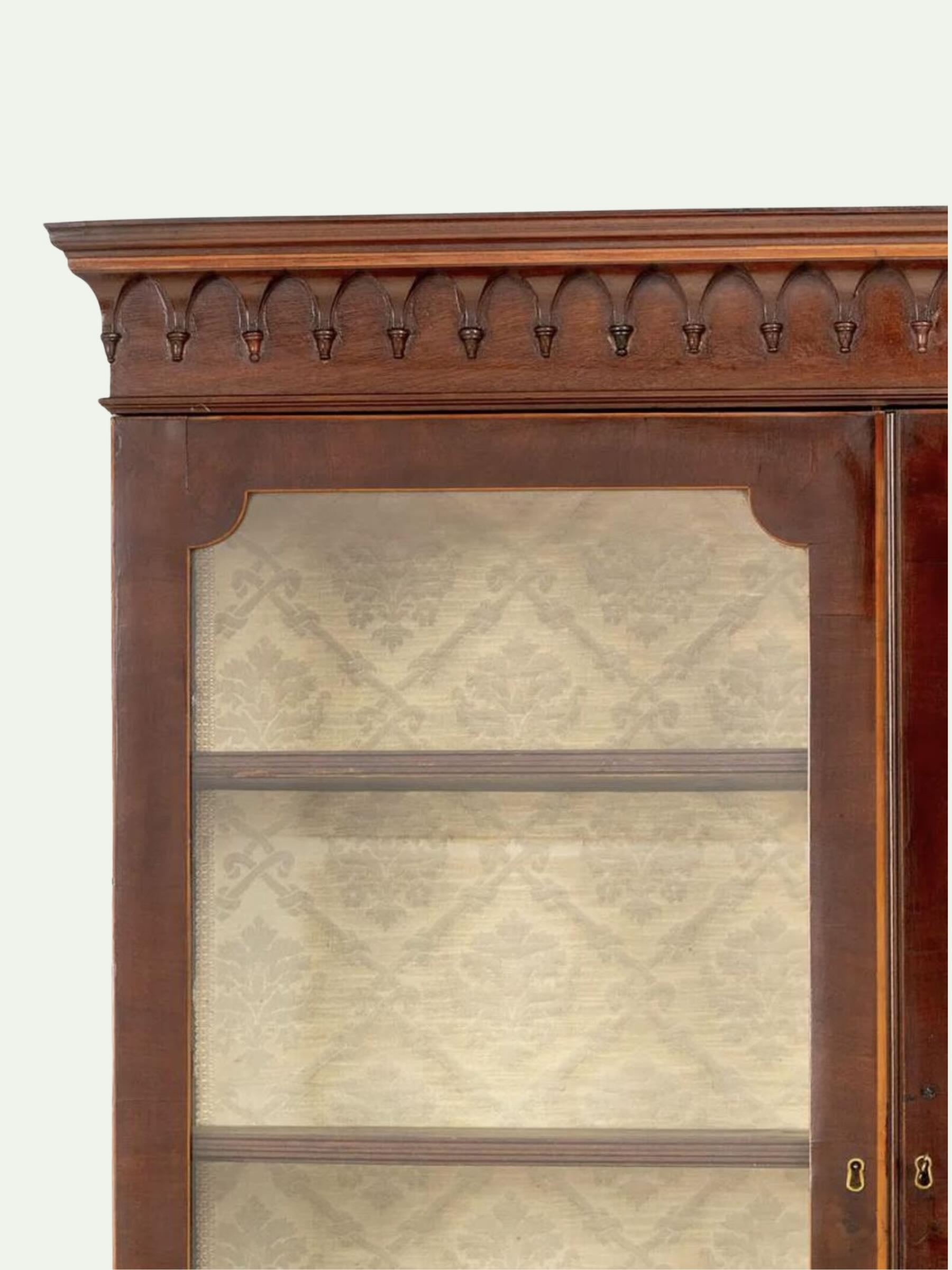 Close-up of a dark reddish-brown wooden display cabinet with a decorative carved top frame and glass doors showing patterned beige lining.
