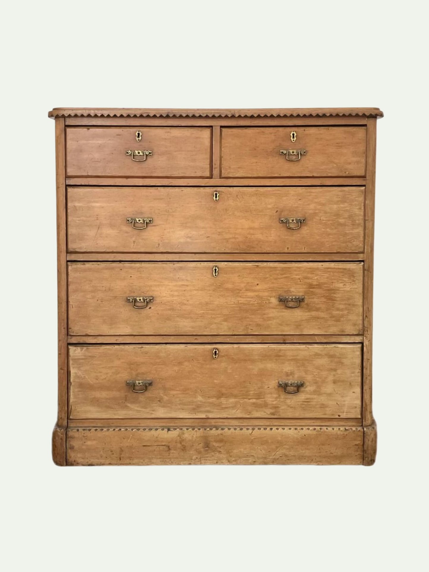An antique wooden five-drawer chest with a warm honey-toned finish, featuring brass drawer pulls and a decorative beaded top and bottom trim, set against a plain off-white background.