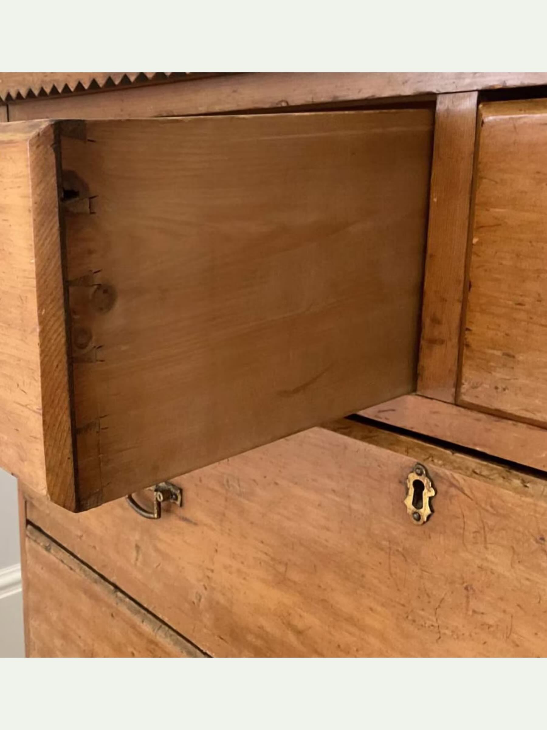 Close-up of a wooden chest of drawers with one drawer pulled open, showing the wood grain and brass hardware.