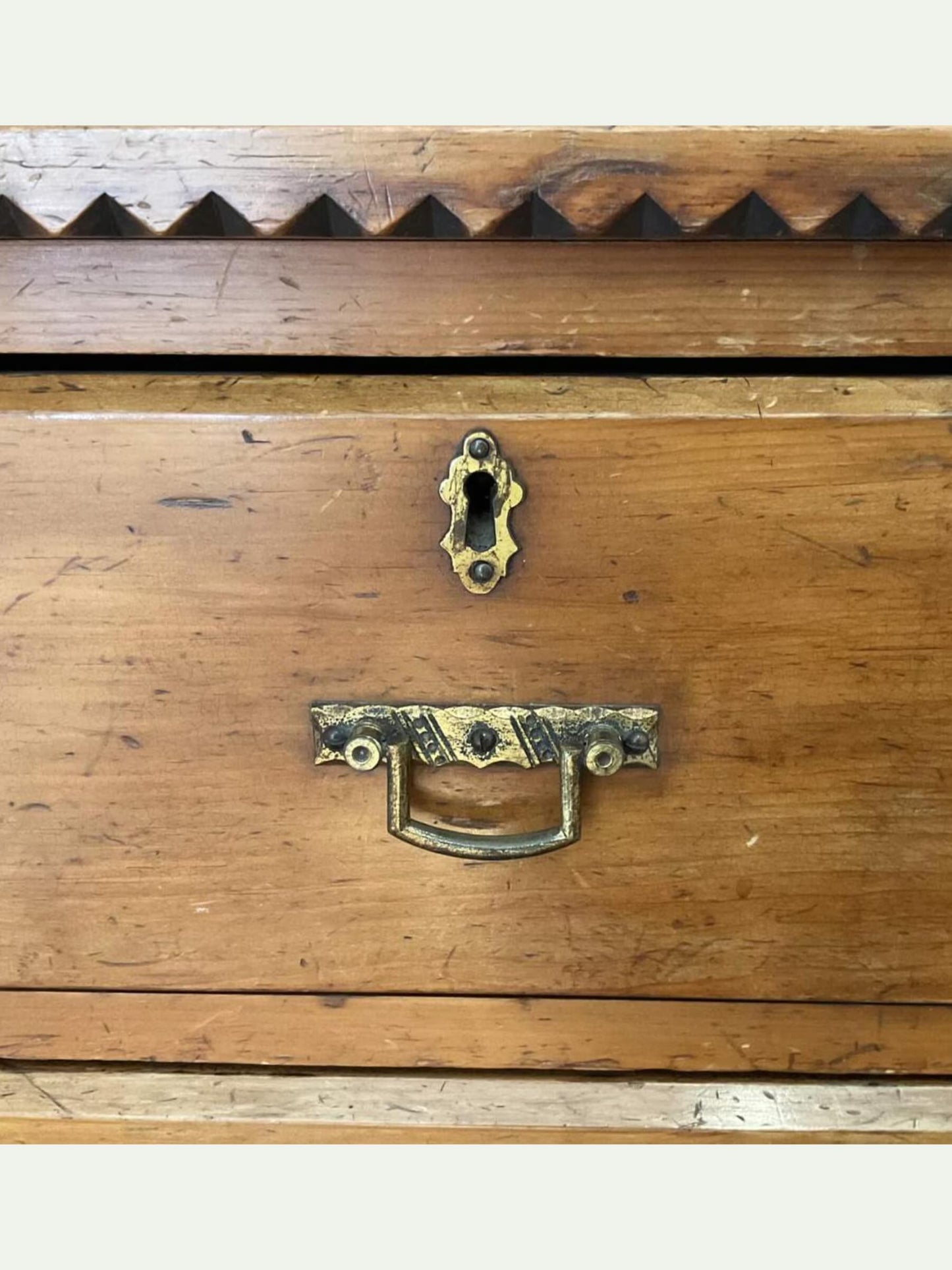 Close-up of a rustic wooden drawer front with an aged brass keyhole and matching pull handle, showing visible wood grain and wear.