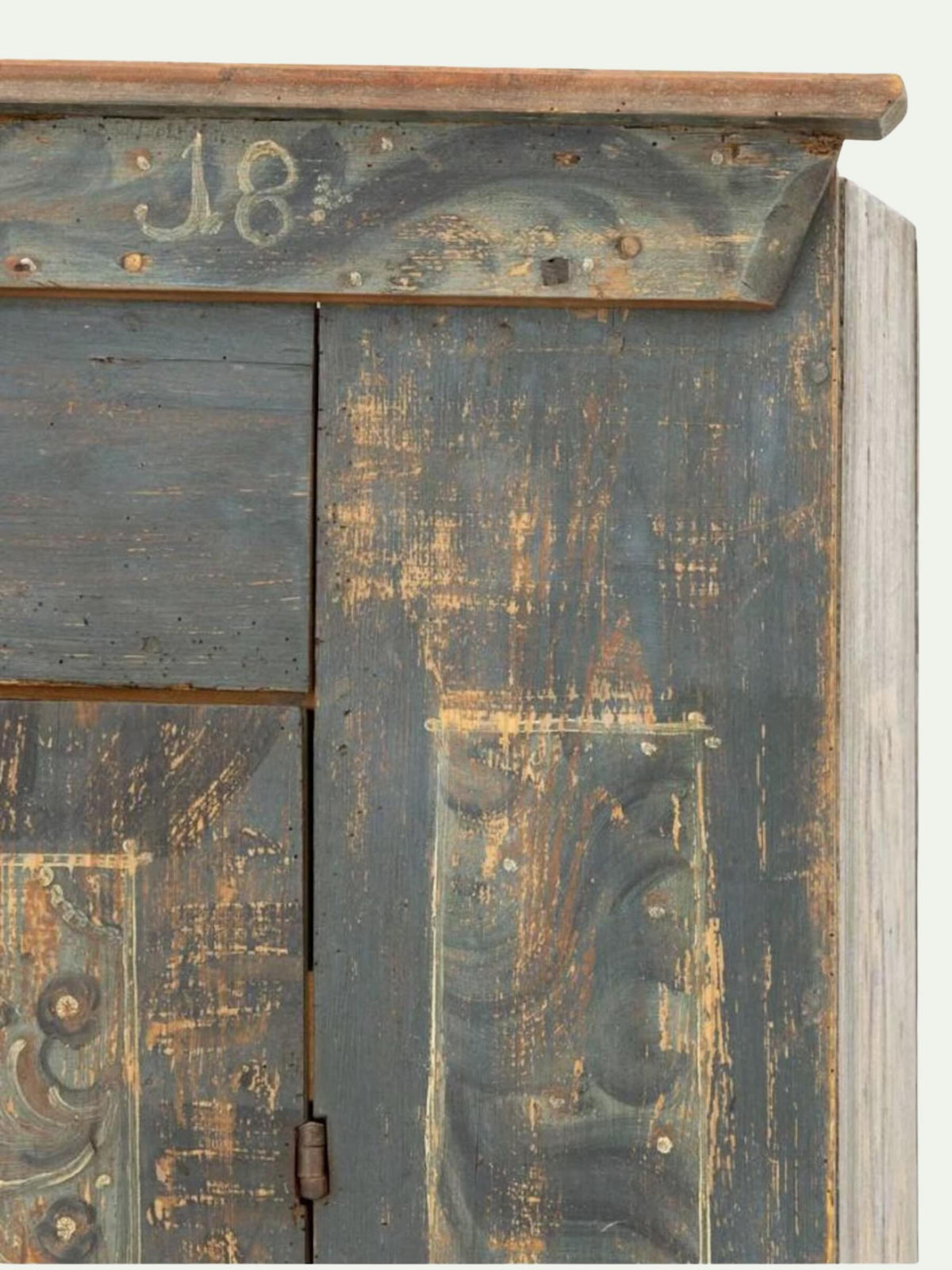 Close-up of a distressed dark blue-gray wooden cabinet with peeling paint, showing weathered wood grain, brass hardware, and the number 18 painted on the top panel.