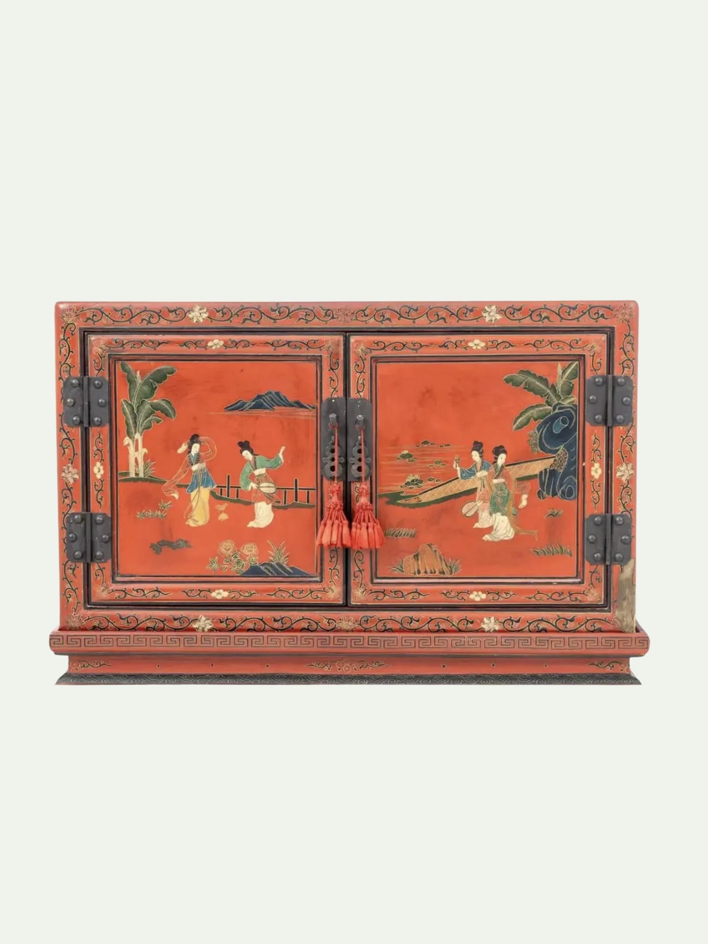 A traditional Chinese lacquered cabinet with a vibrant red-orange finish and hand-painted scenes of figures on a boat and by a palm tree. The cabinet features black metal hinges and decorative tassel pulls, set against a solid off-white background.