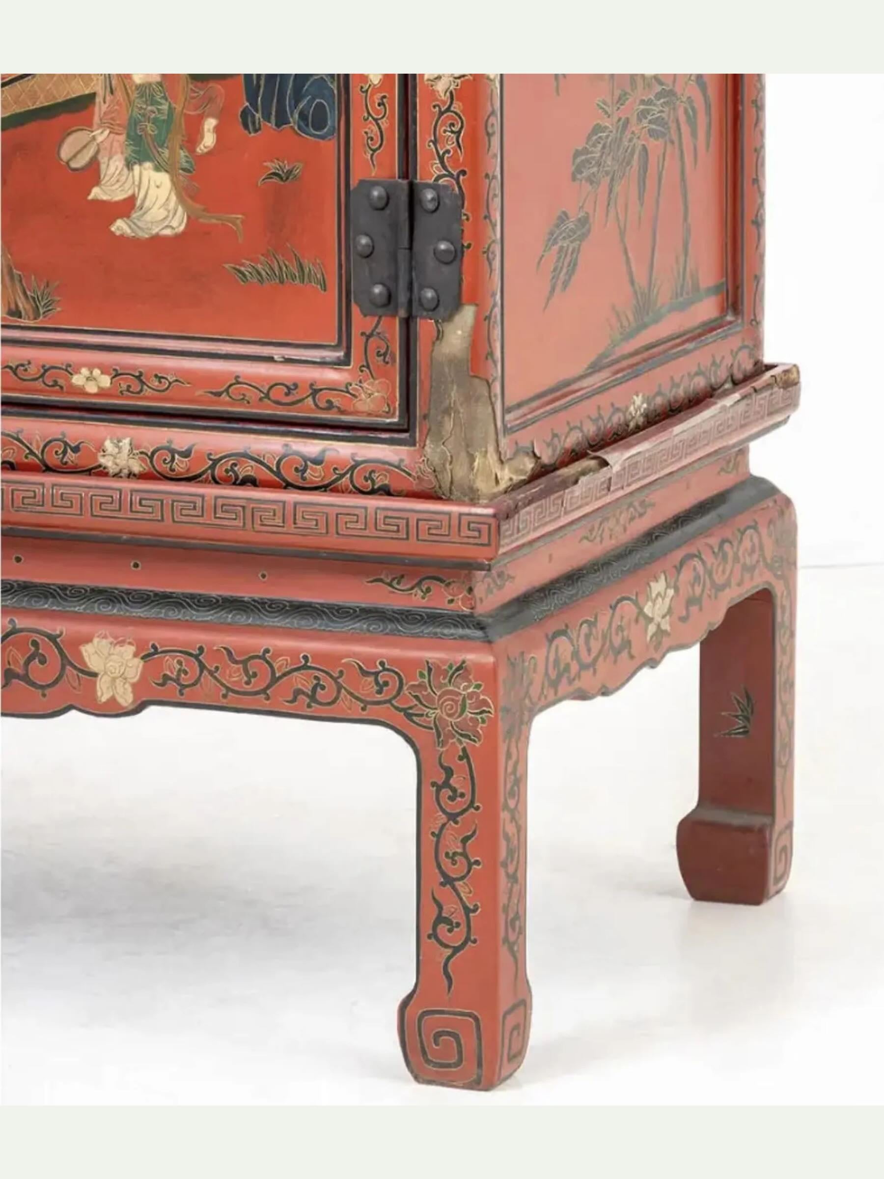 Close-up of a red painted wooden cabinet or side table with black decorative scrollwork and hand-painted floral and scenic motifs on the panels and legs.