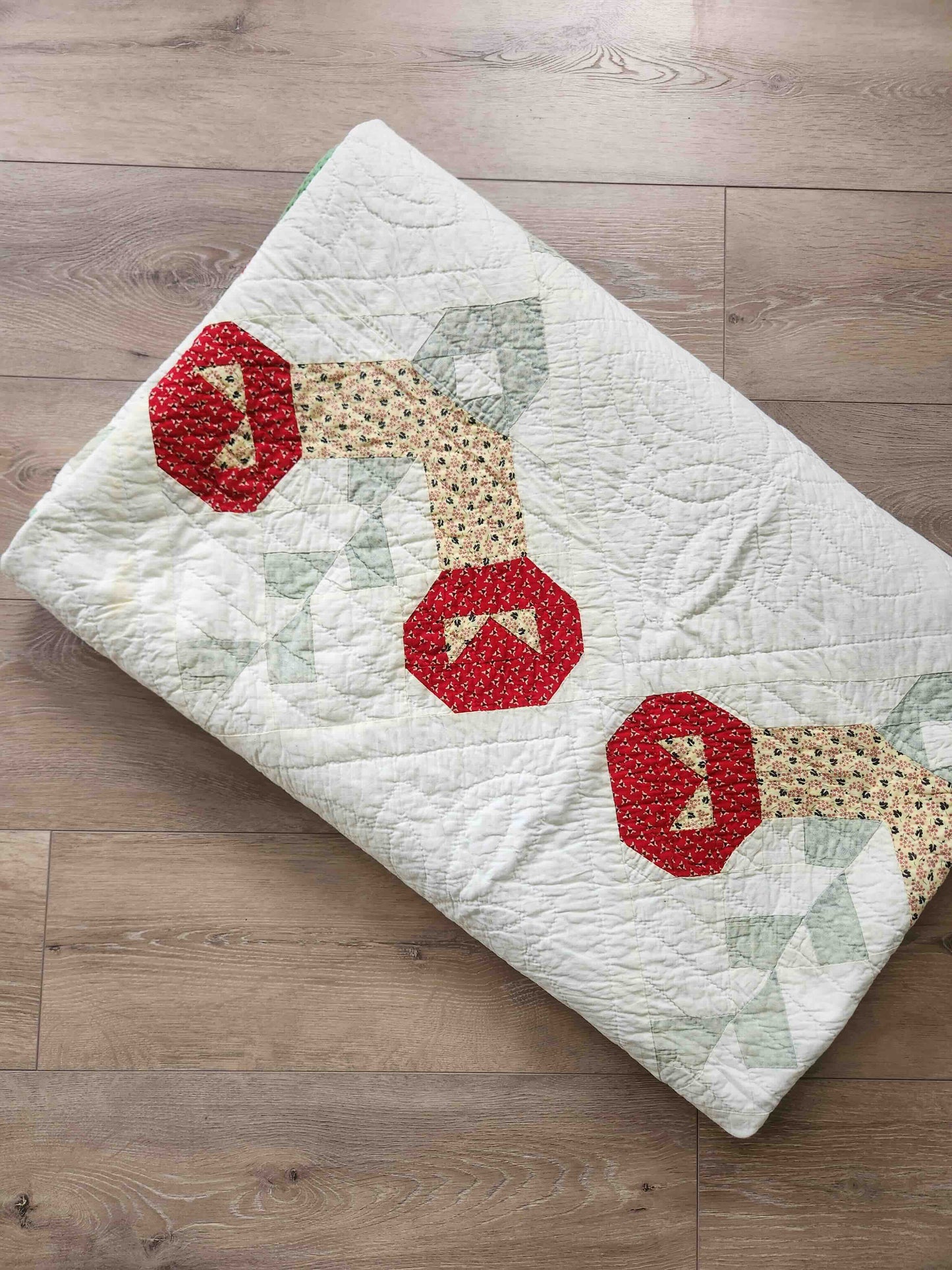 Quilt with red and beige geometric patterns on a wooden floor