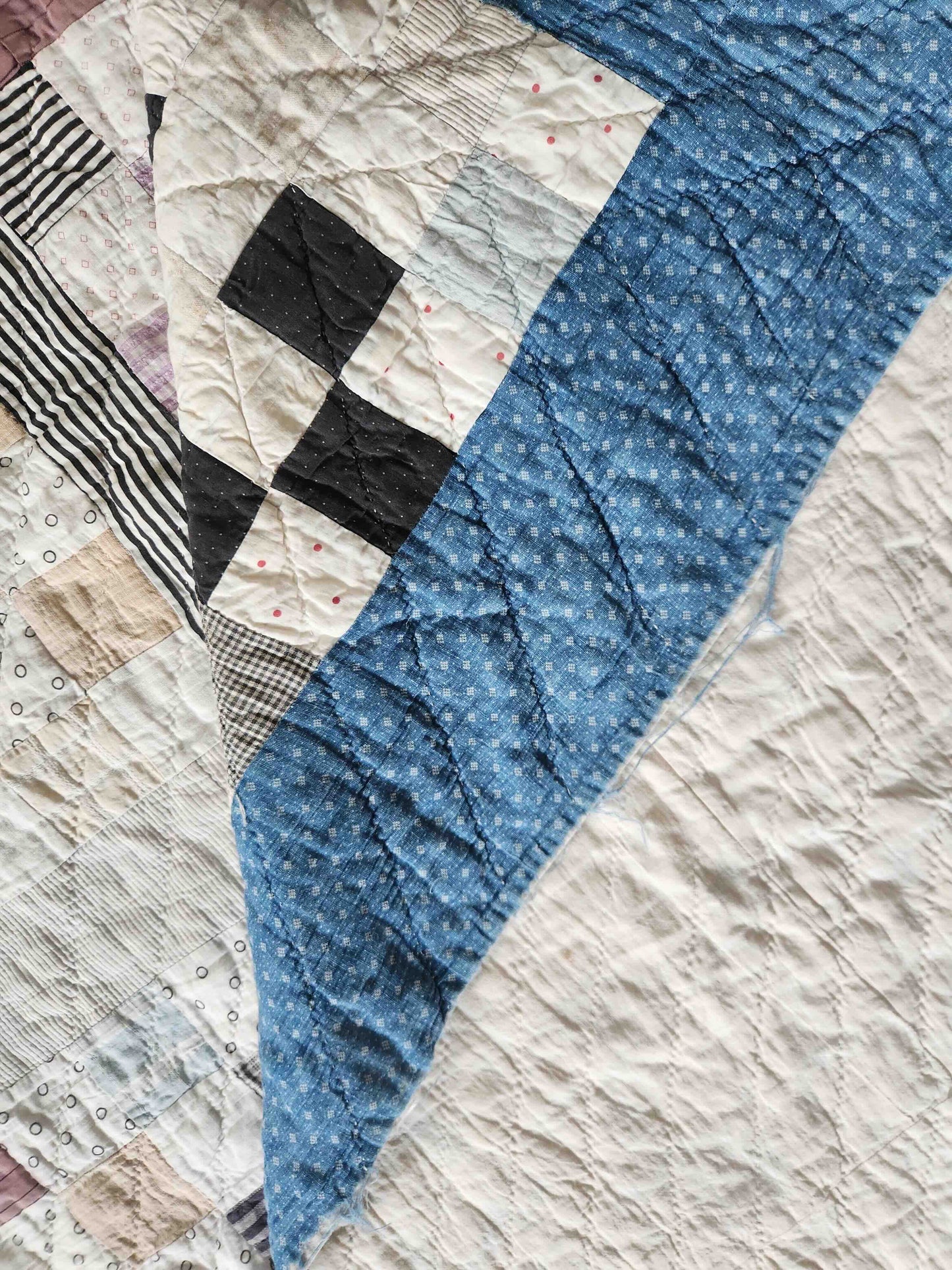 Patchwork quilt with blue, black, and beige patterns on a textured surface