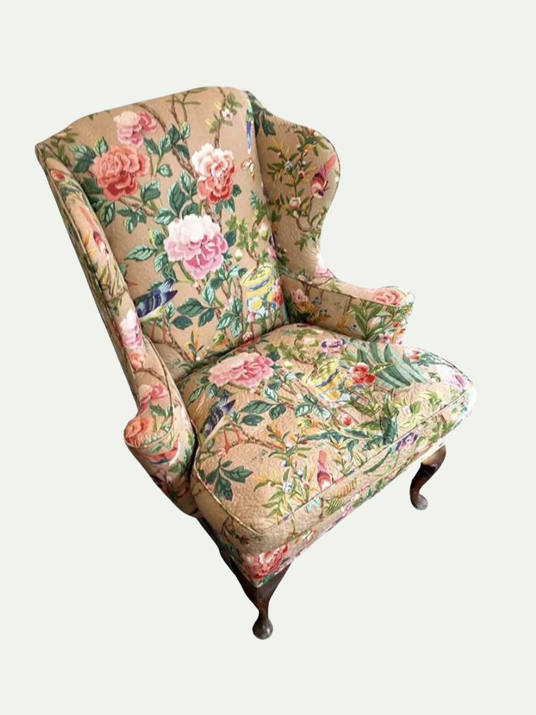 A vintage-style wingback armchair upholstered in a beige fabric with a colorful floral print featuring pink roses, green leaves, and small birds, shown against a plain light background.