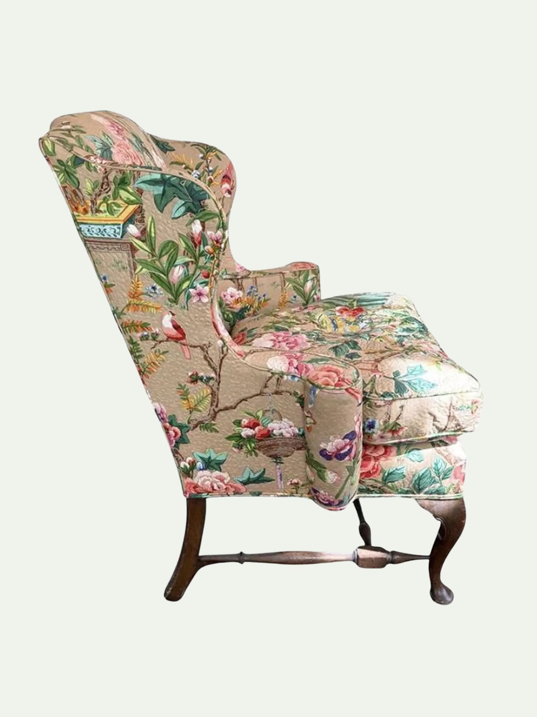 A vintage-style wingback armchair upholstered in a detailed botanical and bird patterned fabric, featuring dark wooden cabriole legs, shown against a solid off-white background.