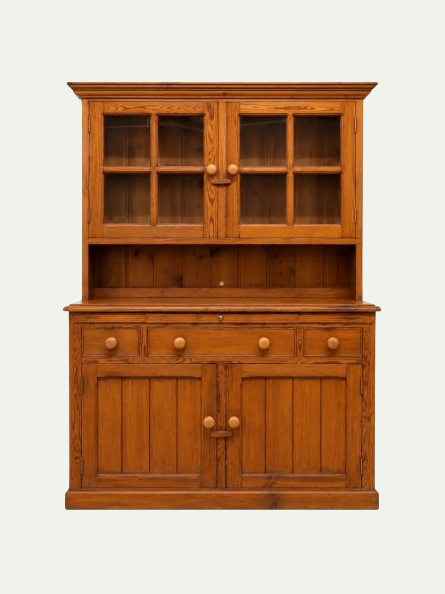 A mid-century modern wooden hutch cabinet in a warm medium brown finish, featuring two upper glass-front doors with six-pane grids, a central open shelf, three drawers with round knobs, and two lower cabinet doors with matching round knobs, set against a plain off-white background.