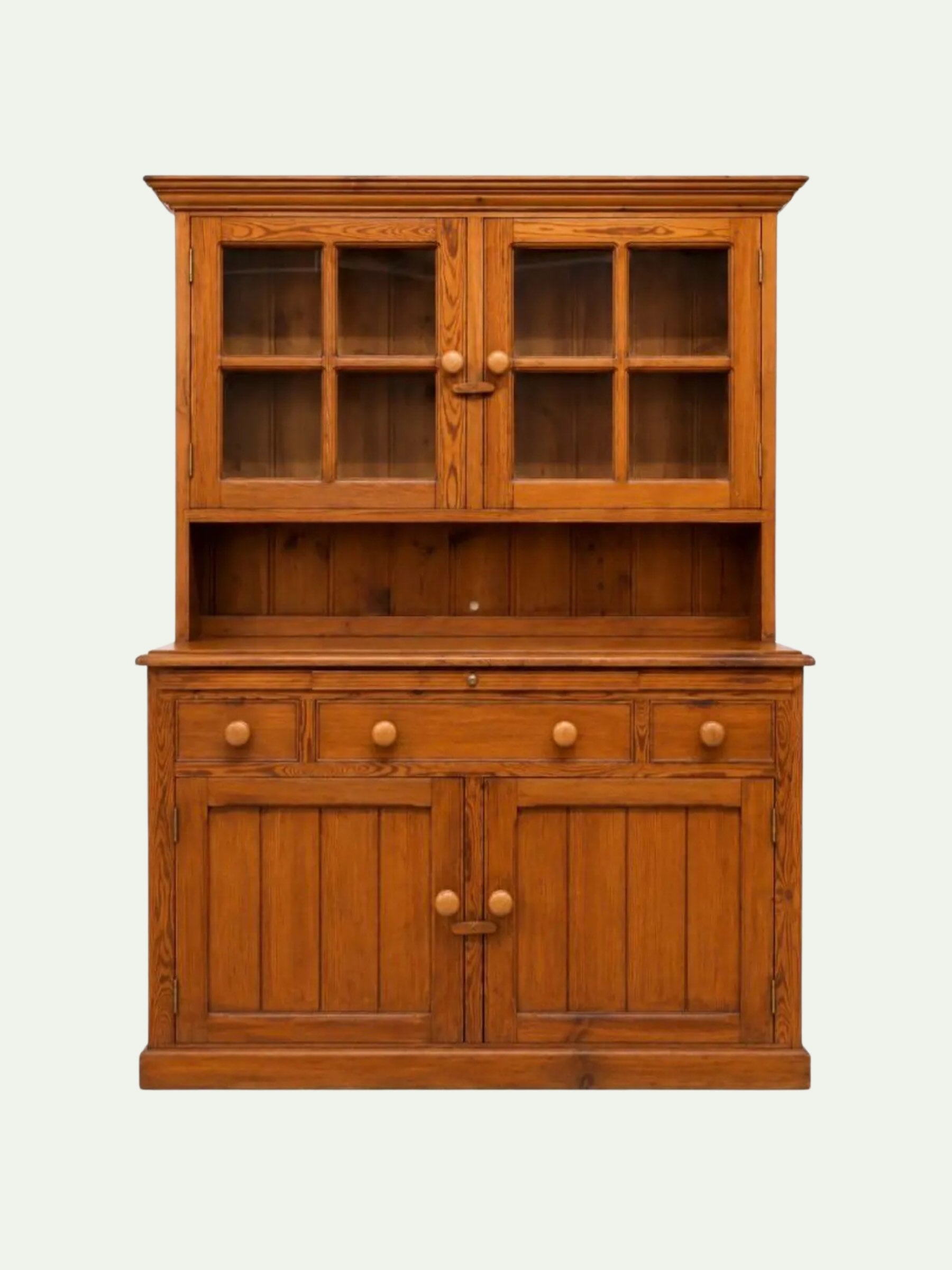 A mid-century modern wooden hutch cabinet in a warm medium brown finish, featuring two upper glass-front doors with six-pane grids, a central open shelf, three drawers with round knobs, and two lower cabinet doors with matching round knobs, set against a plain off-white background.
