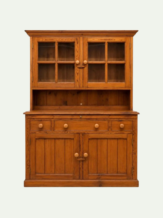 A mid-century modern wooden hutch cabinet in a warm medium brown finish, featuring two upper glass-front doors with six-pane grids, a central open shelf, three drawers with round knobs, and two lower cabinet doors with matching round knobs, set against a plain off-white background.