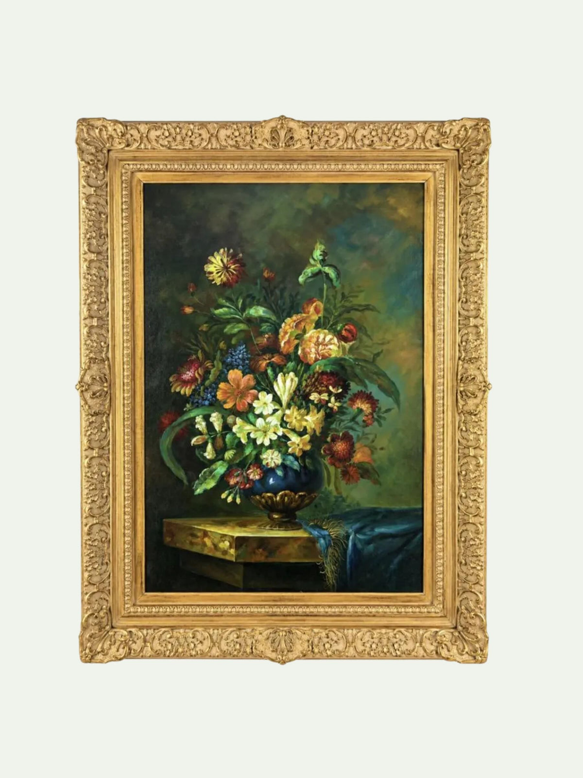 A framed still life painting featuring a vibrant bouquet of flowers in a blue vase on a table, enclosed in an ornate gold frame against a light gray background.