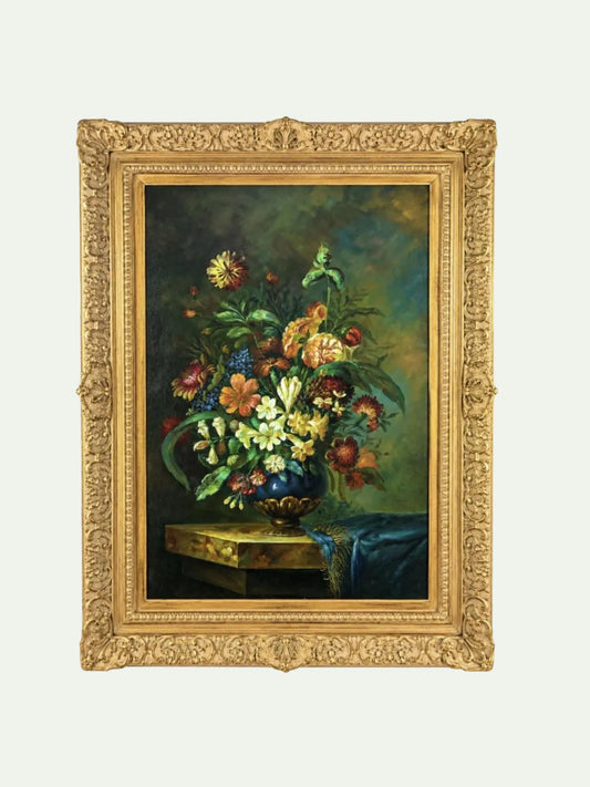 A framed still life painting featuring a vibrant bouquet of flowers in a blue vase on a table, enclosed in an ornate gold frame against a light gray background.