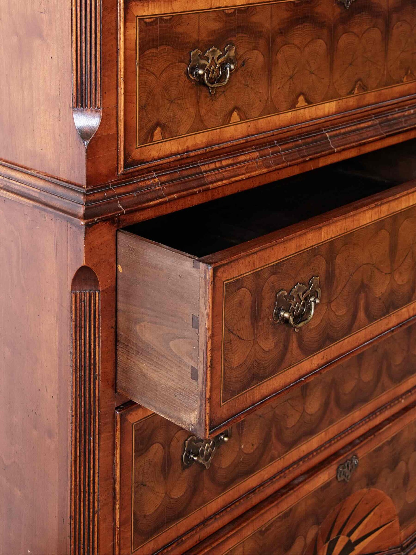 Close-up of an antique wooden chest of drawers with a middle drawer pulled open, showing detailed marquise inlay patterns and brass drawer pulls.