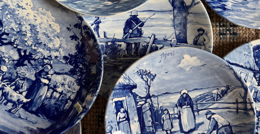 A close-up of several blue-and-white ceramic plates featuring hand-painted rural landscape scenes with figures, trees, and farm animals.
