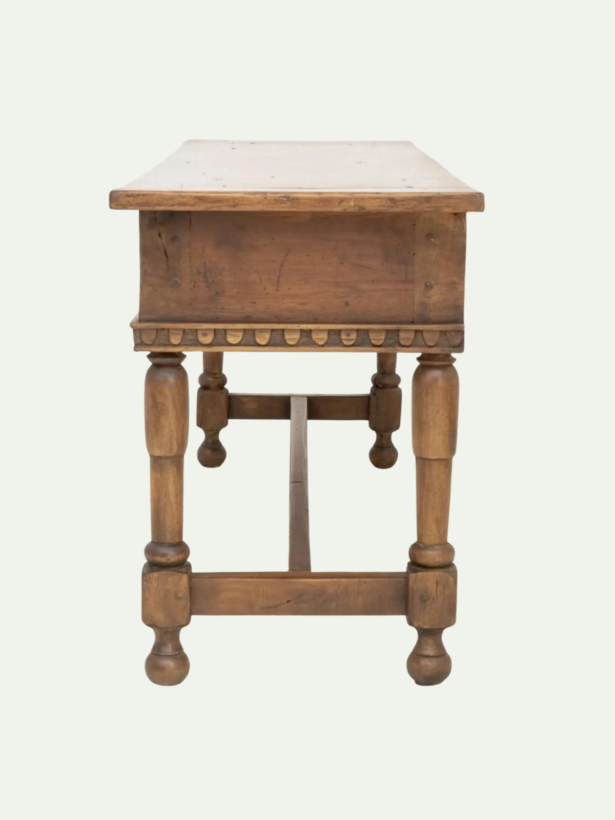 A rustic wooden writing desk with turned legs and a decorative apron, shown from the front on a light off-white background.