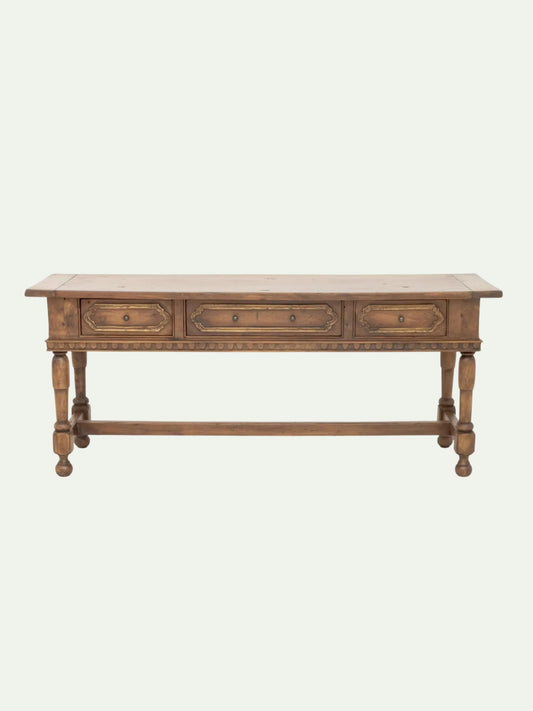A rustic wooden console table with three drawers, turned legs, and a lower stretcher bar, shown against a plain off-white background.