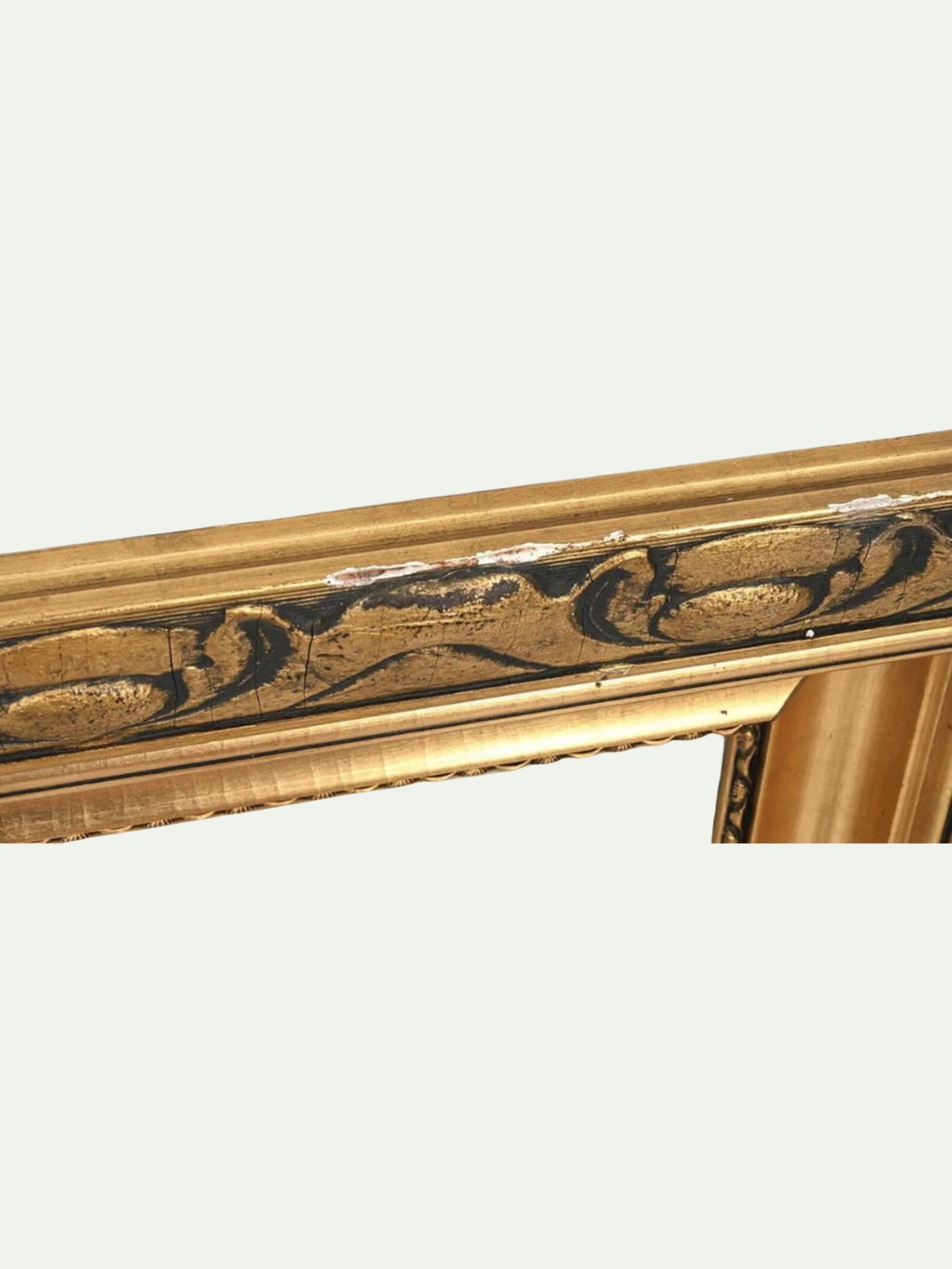 Close-up of an ornate gold picture frame with carved scrollwork and a distressed finish, shown against a plain off-white background.