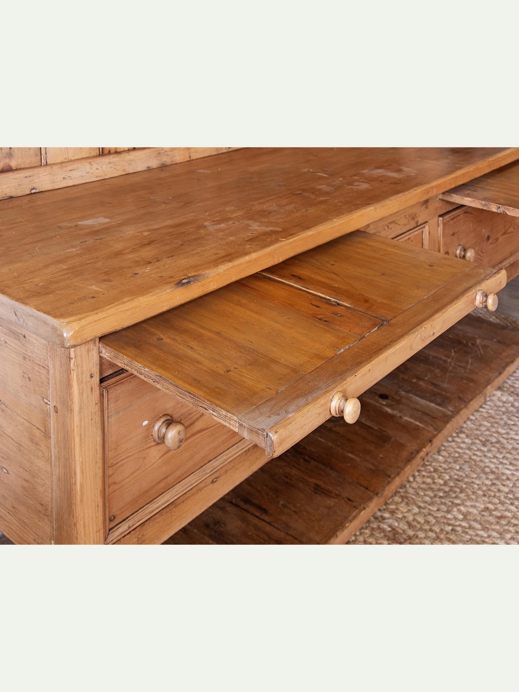 A rustic wooden chest of drawers with a warm medium-brown finish, featuring an open middle drawer and small round wooden knobs, set against a light off-white background.