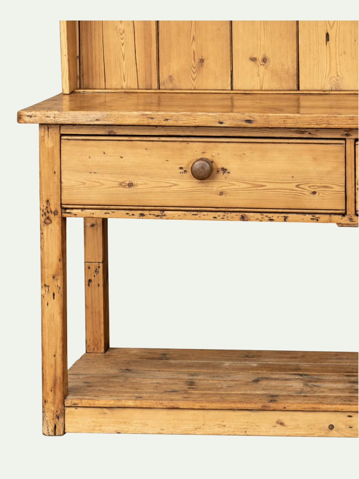 A rustic pine wooden writing desk with a single drawer featuring a round wooden knob, a lower shelf, and a matching wooden back panel, shown against a plain off-white background.