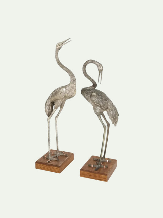 Two metallic bird sculptures on wooden bases against a white background