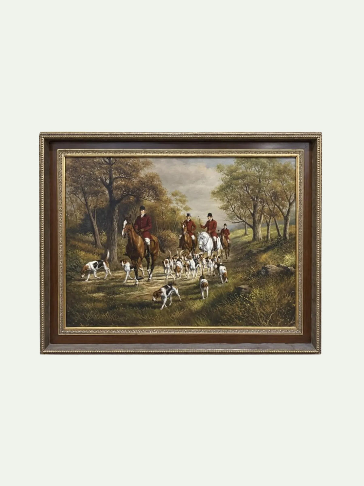 A framed landscape painting depicting a fox hunting scene with riders on horseback and hounds in a wooded clearing, shown against a plain light background.