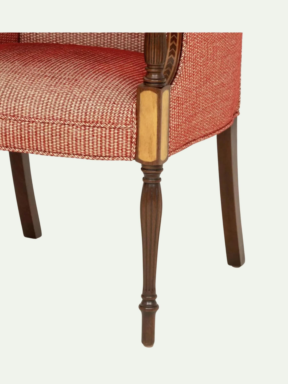 Close-up of an upholstered chair showing the textured rust-red fabric seat and back, a turned dark wood armrest with a light wood inlay, and the front of a dark wood leg on a light gray background.