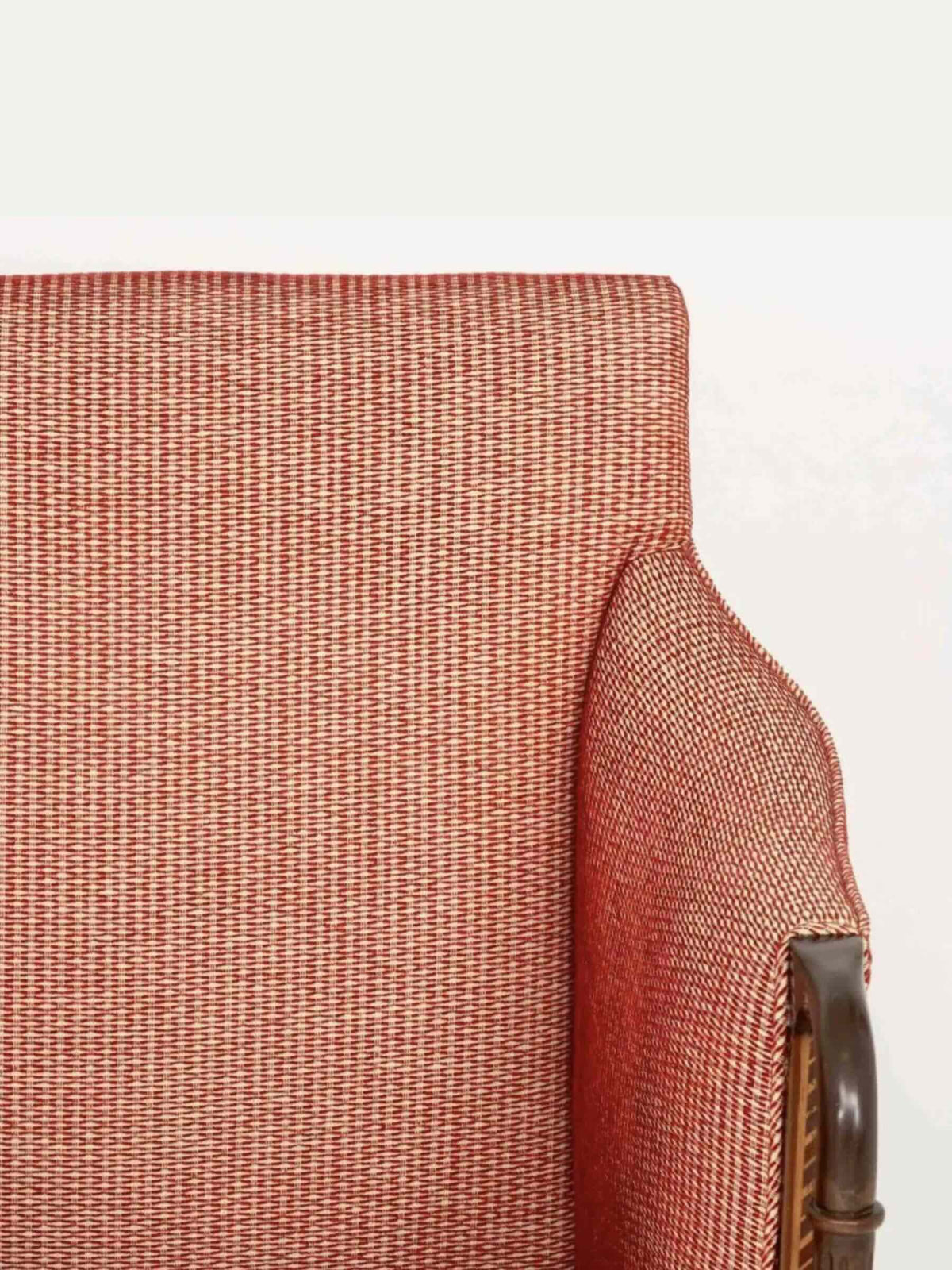 Close-up of a textured woven upholstery fabric in a warm rust-orange color, showing the fabric detail and a small portion of a dark wooden armrest.