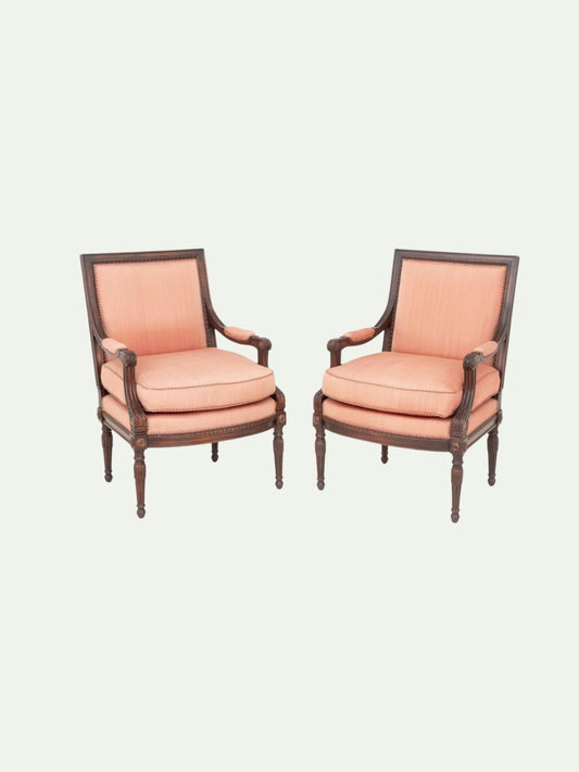 A pair of classic French provincial style armchairs with dusty pink upholstered seats and backrests, set against a solid off-white background.