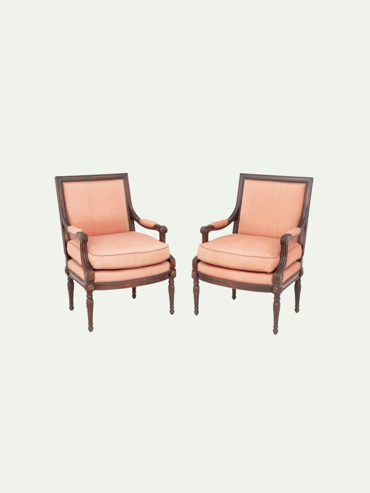 A pair of classic French-style armchairs with dusty pink upholstery and dark brown wooden frames, set against a solid off-white background.
