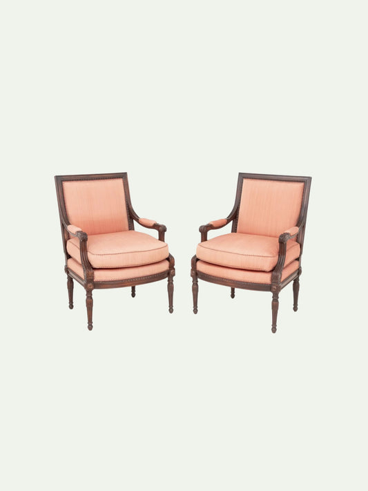 A pair of classic French-style armchairs with dusty pink upholstery and dark brown wooden frames, set against a solid off-white background.