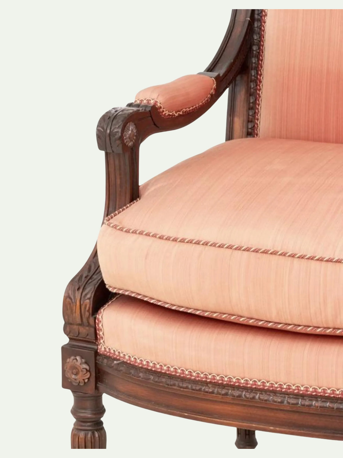 Close-up of a classic French provincial armchair featuring dusty pink striped upholstery and carved dark brown wooden arms and legs.