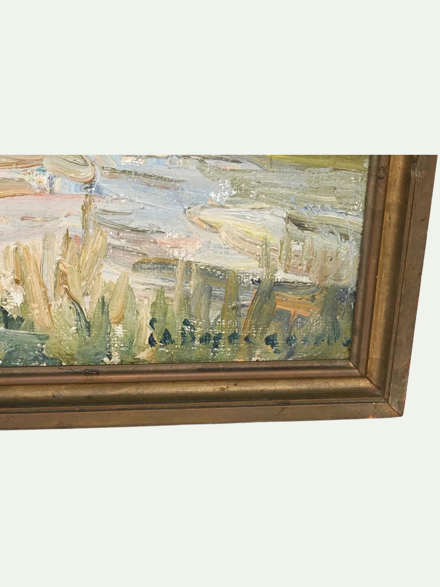 A close-up of a framed landscape painting showing textured brushstrokes of green, beige, and blue tones, with a thick gold-toned wooden frame visible against a light gray background.
