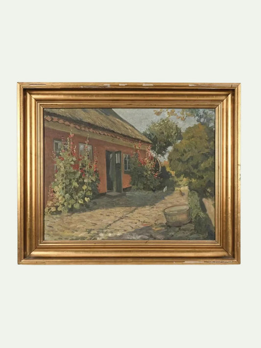 A framed landscape oil painting depicting a rustic red-orange cottage with a stone path, green trees, and climbing flowers, housed in an ornate gold frame against a light gray background.