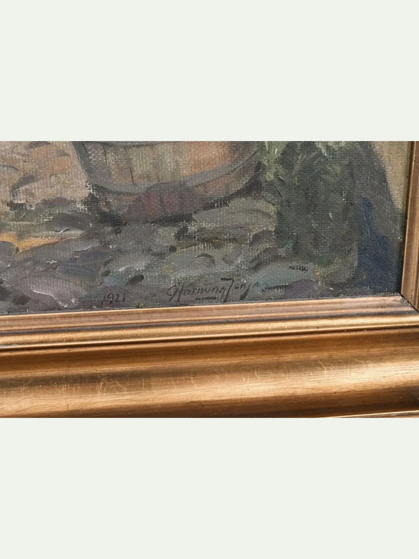 Close-up of a framed painting showing part of a still life scene with a basket and textured brushstrokes, bordered by a gold-toned frame against a light gray background.