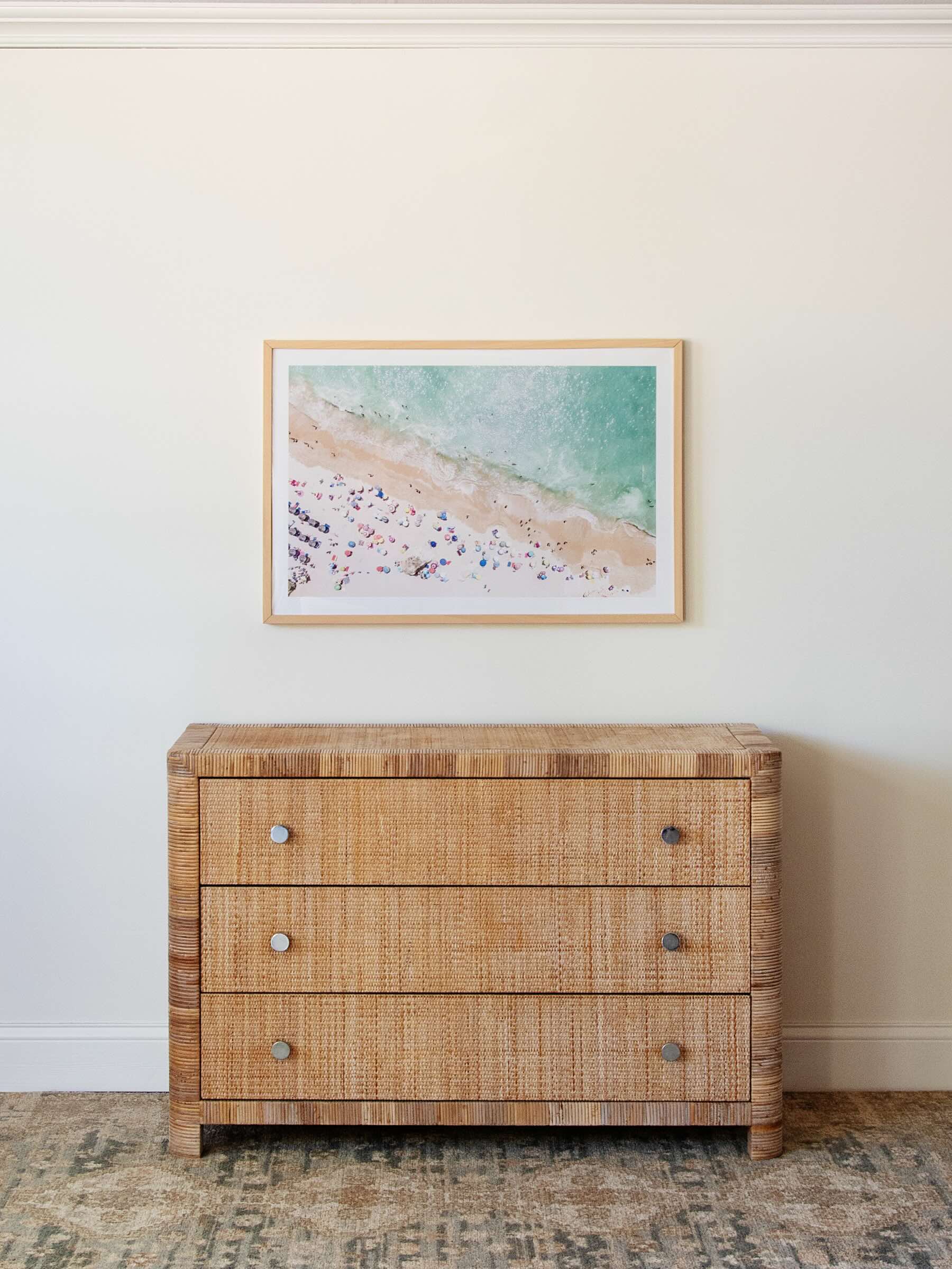 Wicker dresser with a framed beach scene print on a white wall.