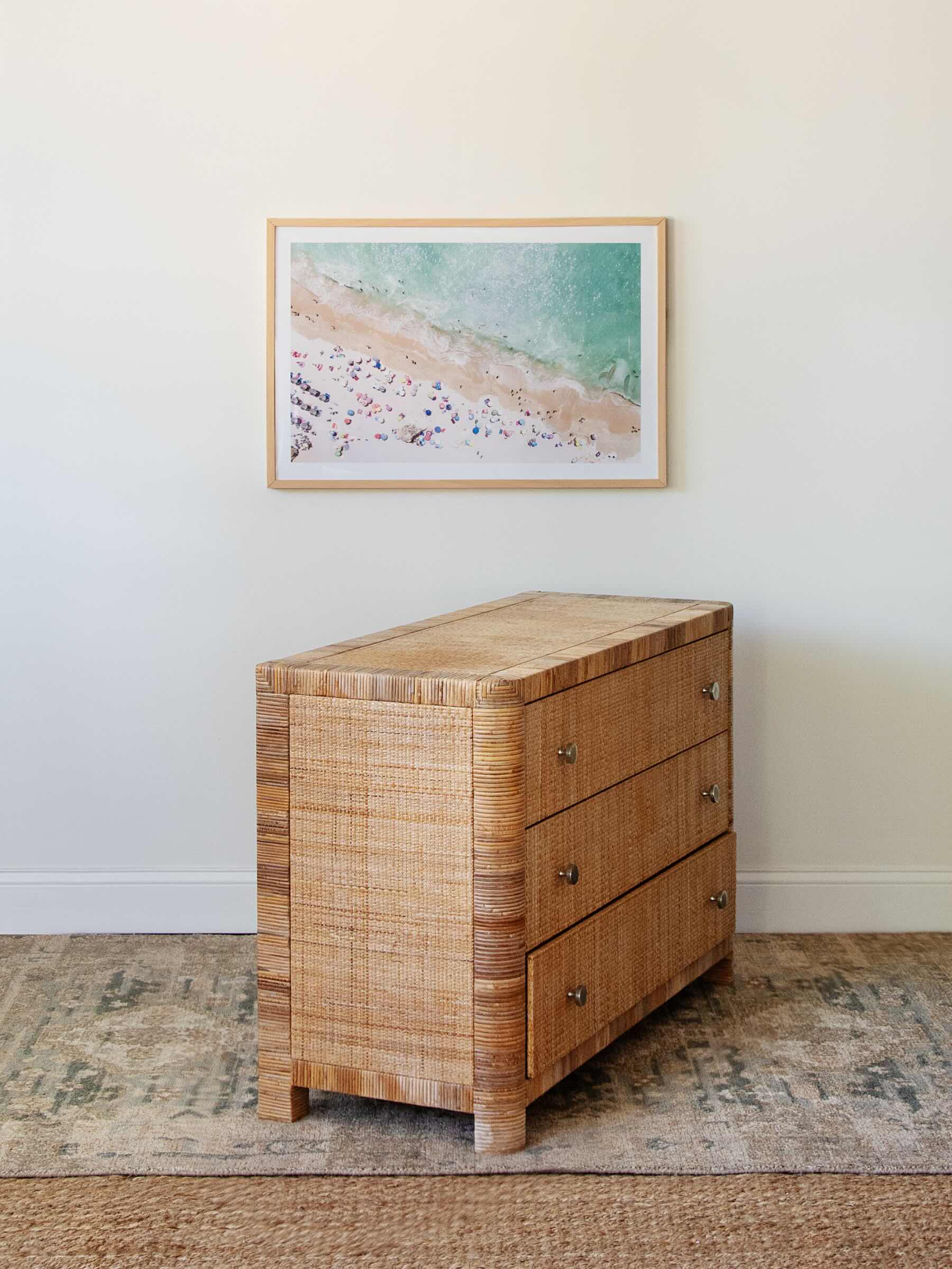 Wicker dresser with framed beach scene artwork on a white wall.