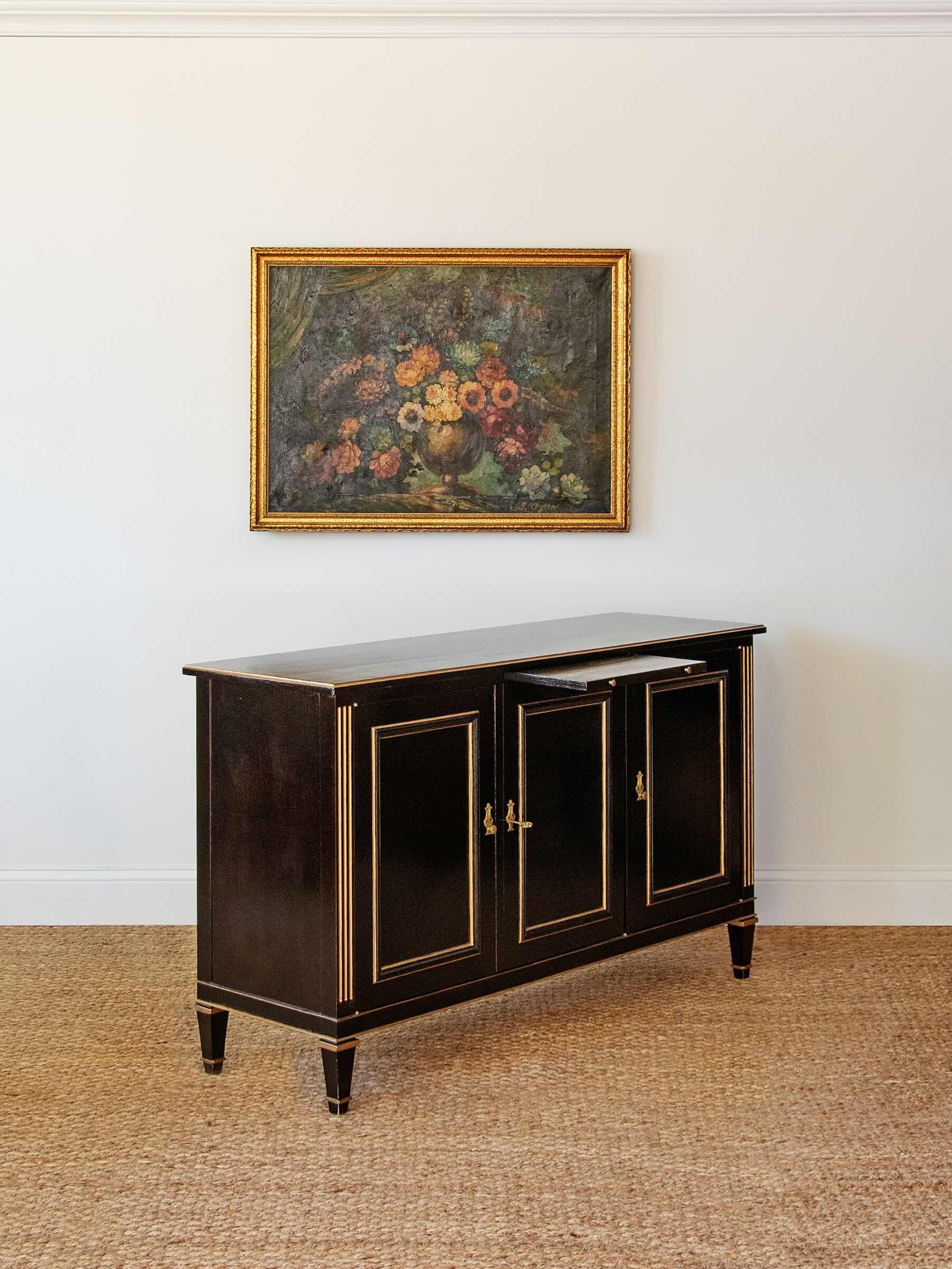 Black cabinet with gold accents in a room with a painting on the wall.